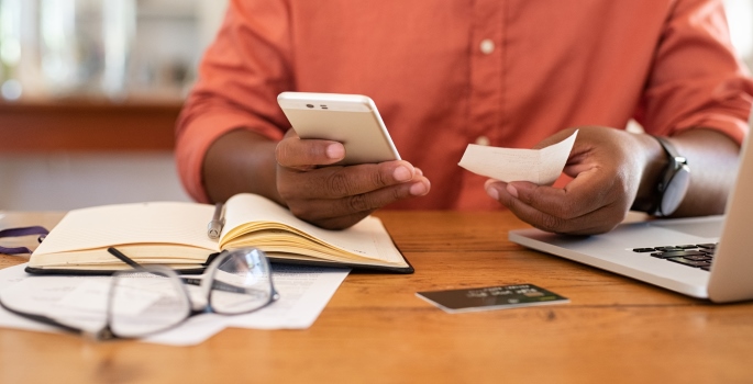 Person holding phone and ticket making online payment with credit card on table