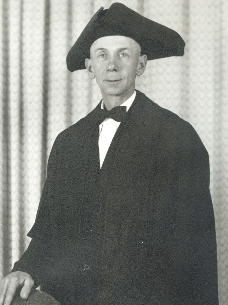 Black and white photo of white male in wardens cap and gown