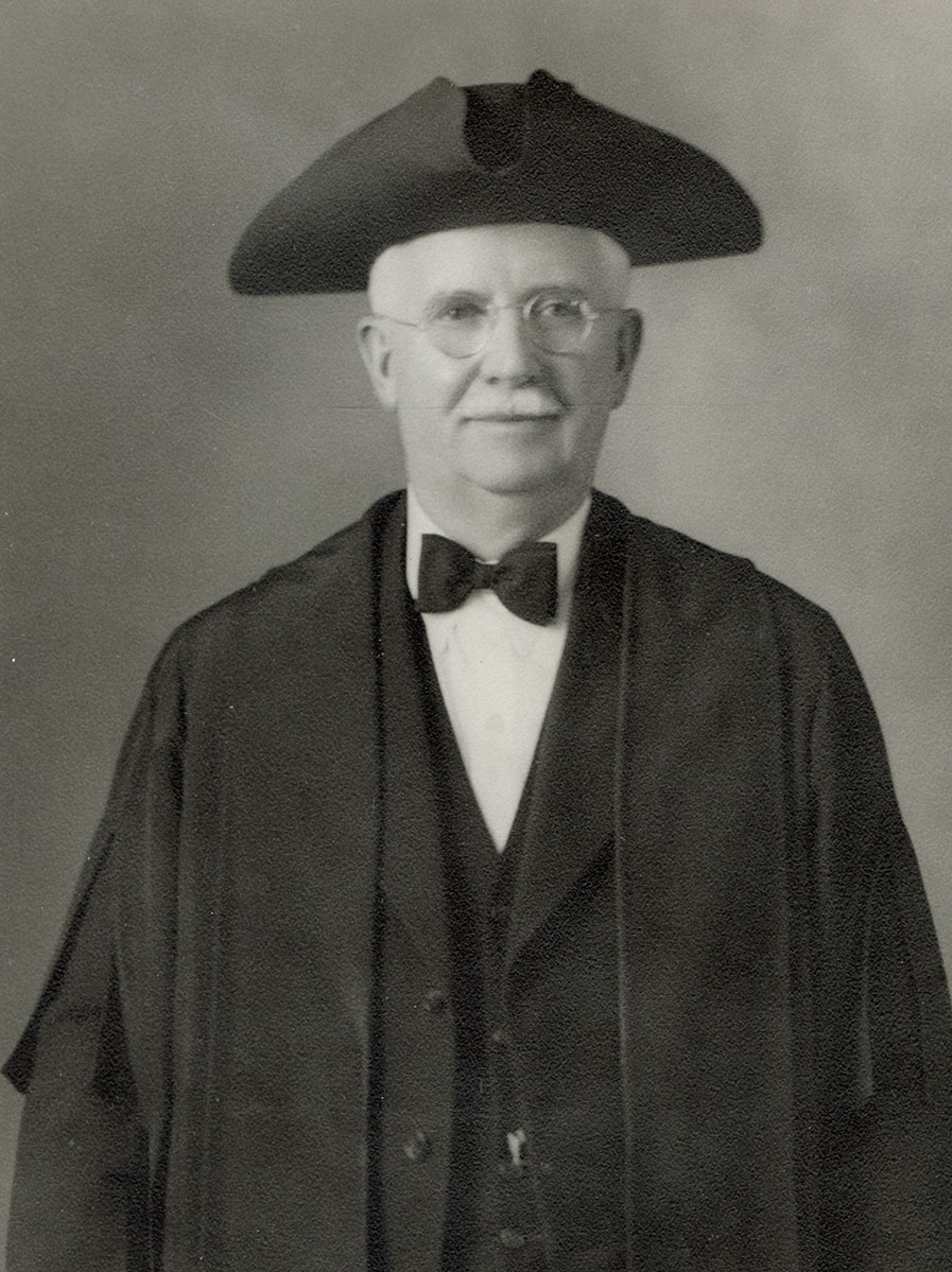 Black and white photo of white male in wardens cap and gown
