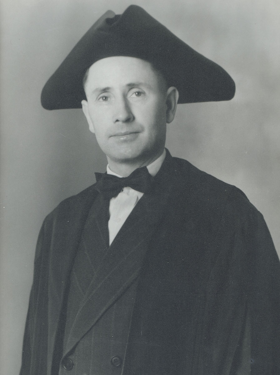 Black and white photo of white male in wardens cap and gown