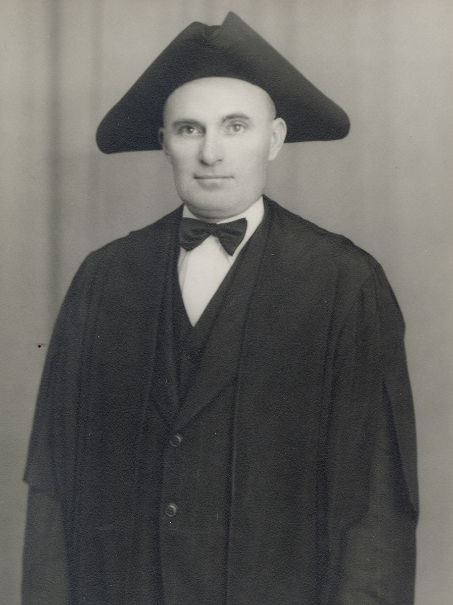 Black and white photo of white male in wardens cap and gown
