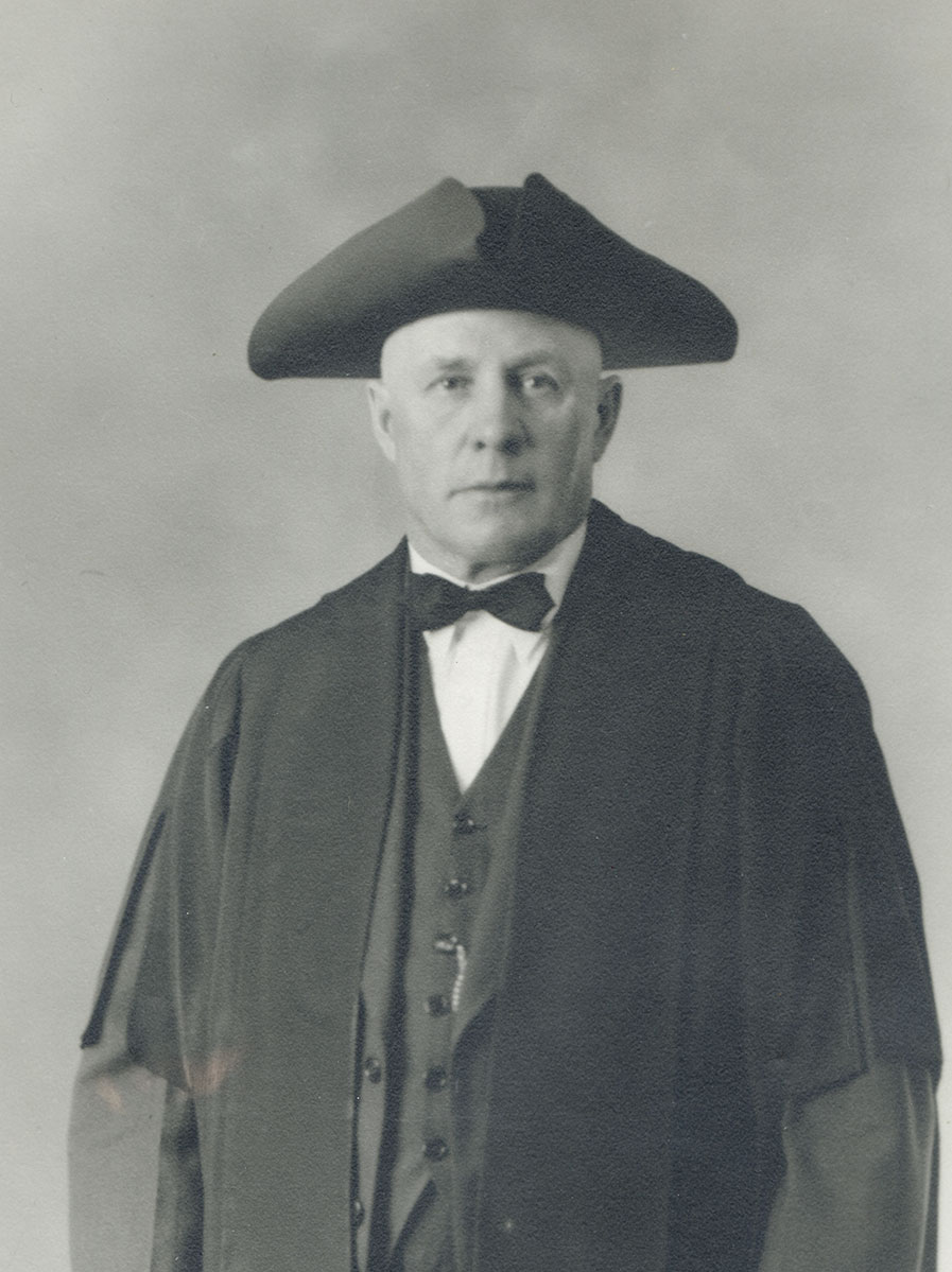 Black and white photo of white male in wardens cap and gown