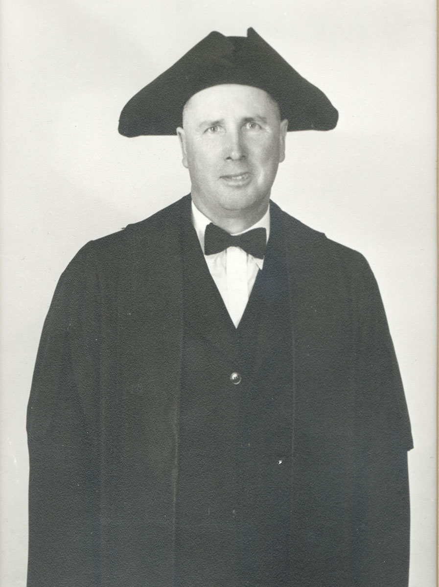 Black and white photo of white male in wardens cap and gown