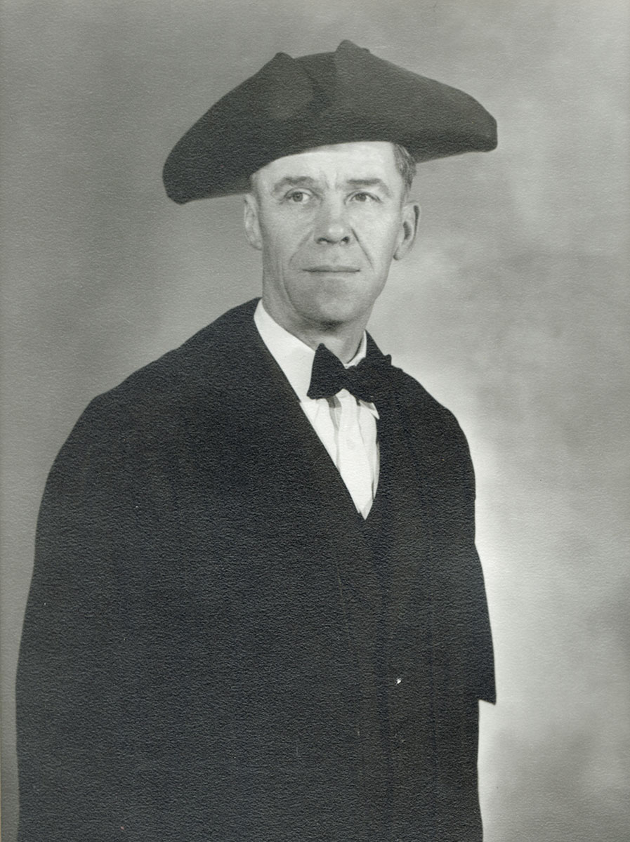 Black and white photo of white male in wardens cap and gown
