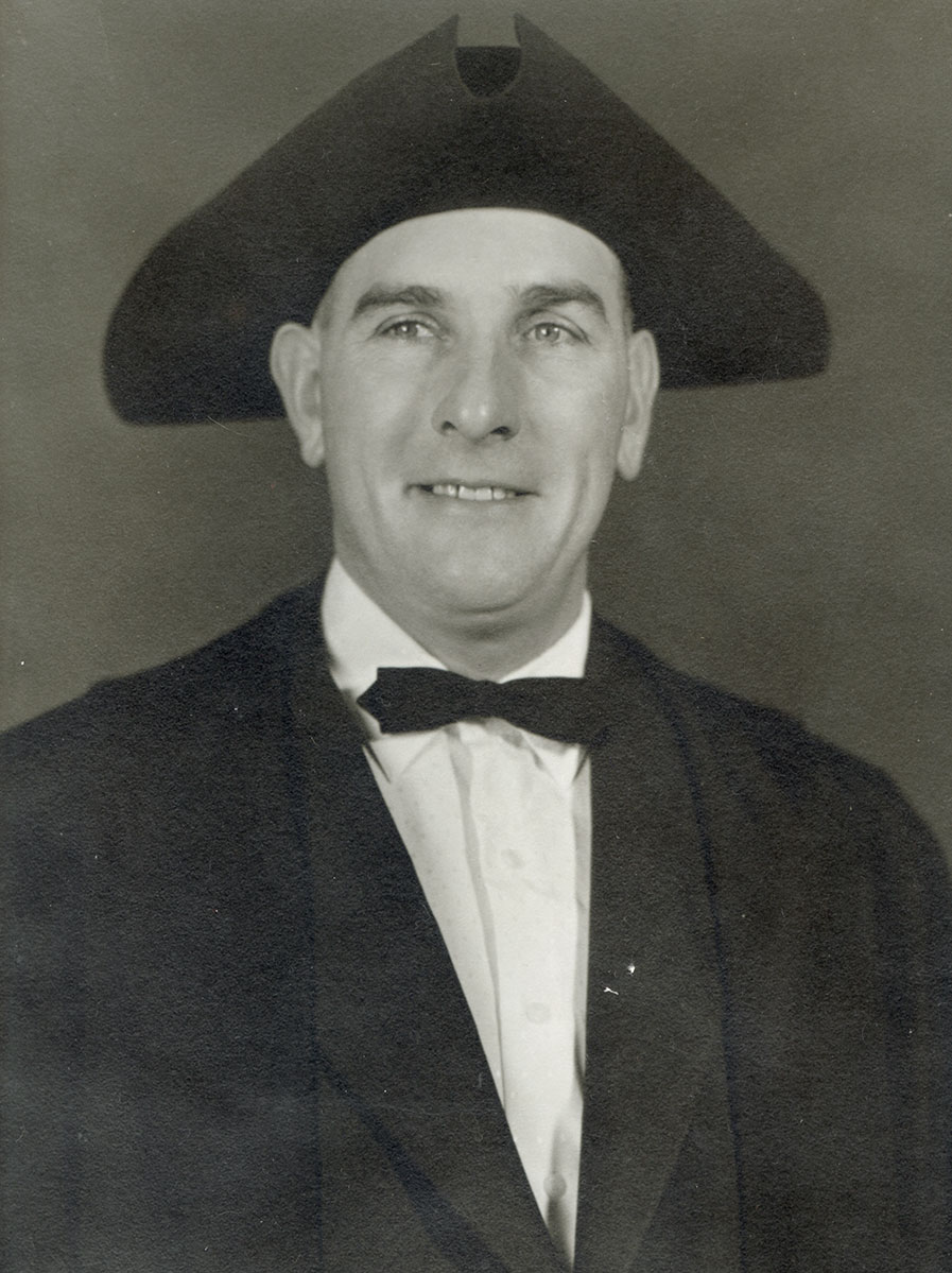 Black and white photo of white male in wardens cap and gown