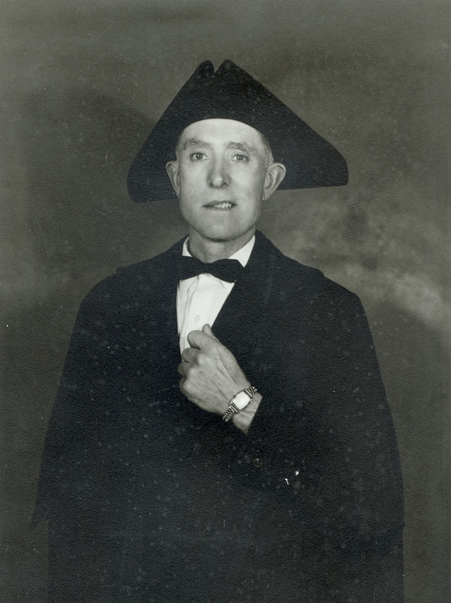 Black and white photo of white male in wardens cap and gown