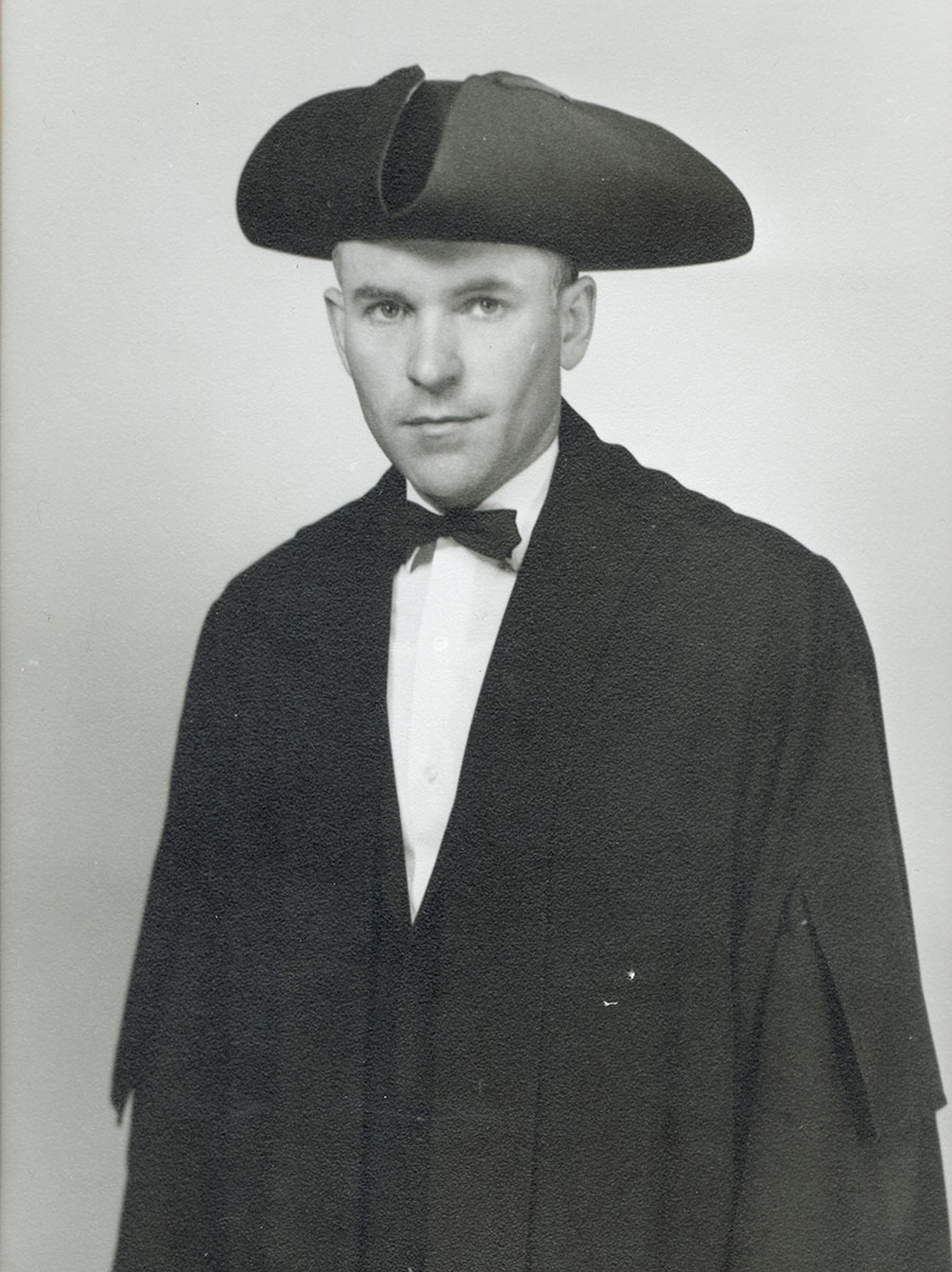 Black and white photo of white male in wardens cap and gown