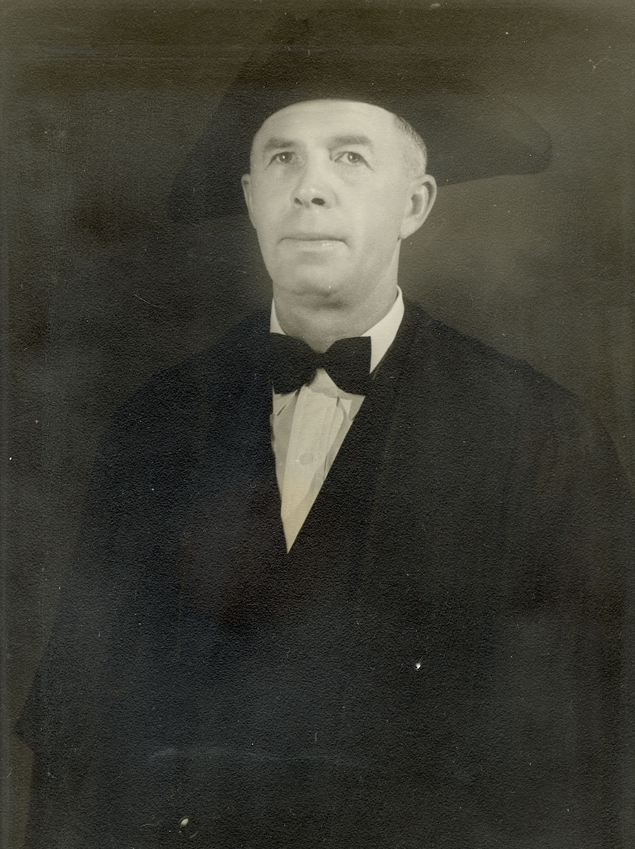 Black and white photo of white male in wardens cap and gown