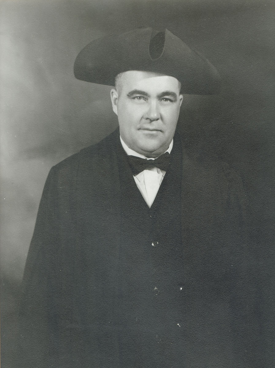 Black and white photo of white male in wardens cap and gown