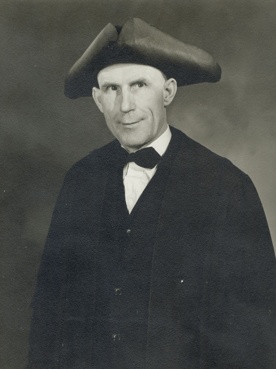 Black and white photo of white male in wardens cap and gown