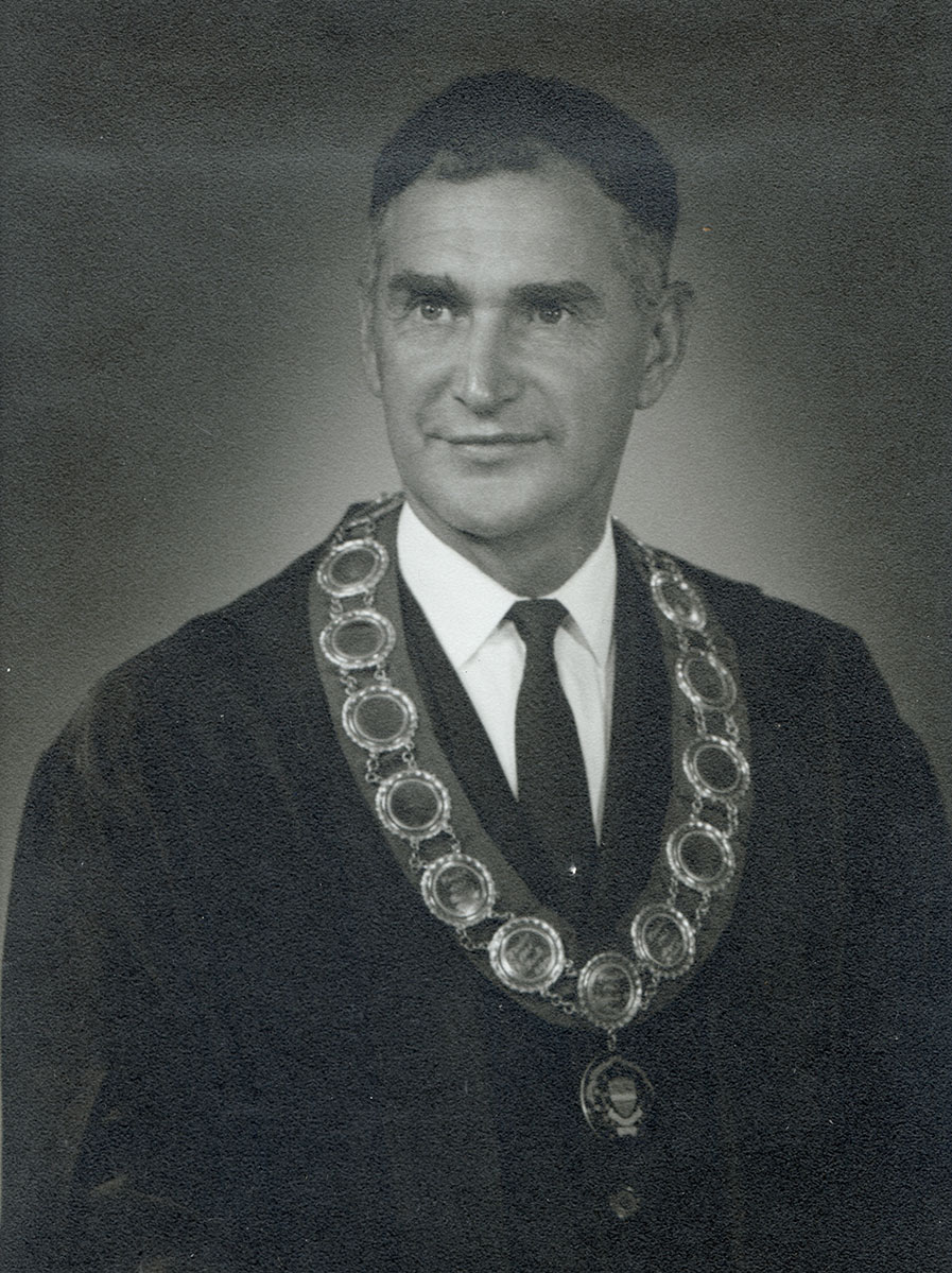Black and white photo of white male in wardens cap and gown