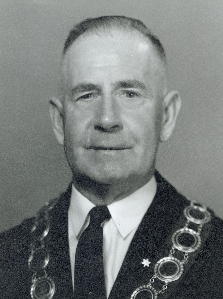 Black and white photo of white male in wardens cap and gown