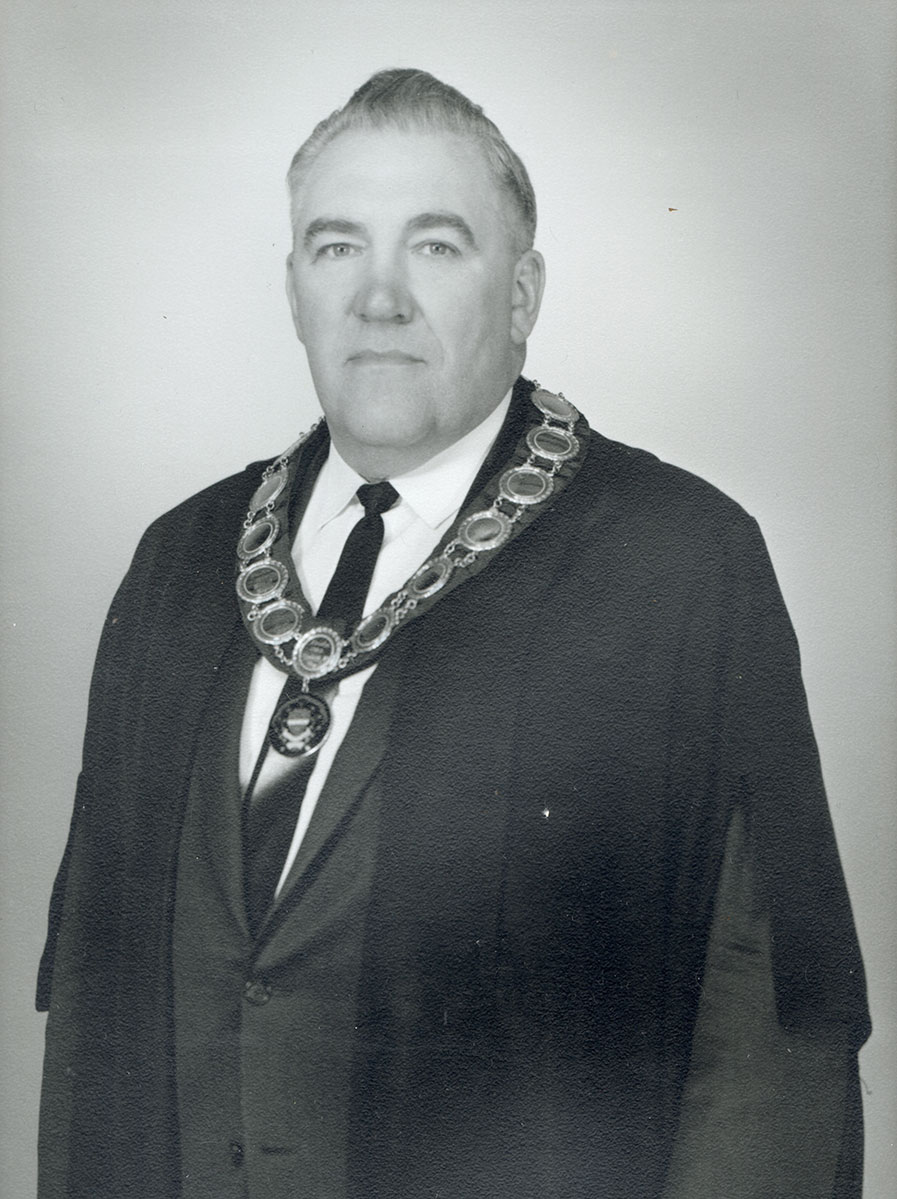 Black and white photo of white male in wardens cap and gown