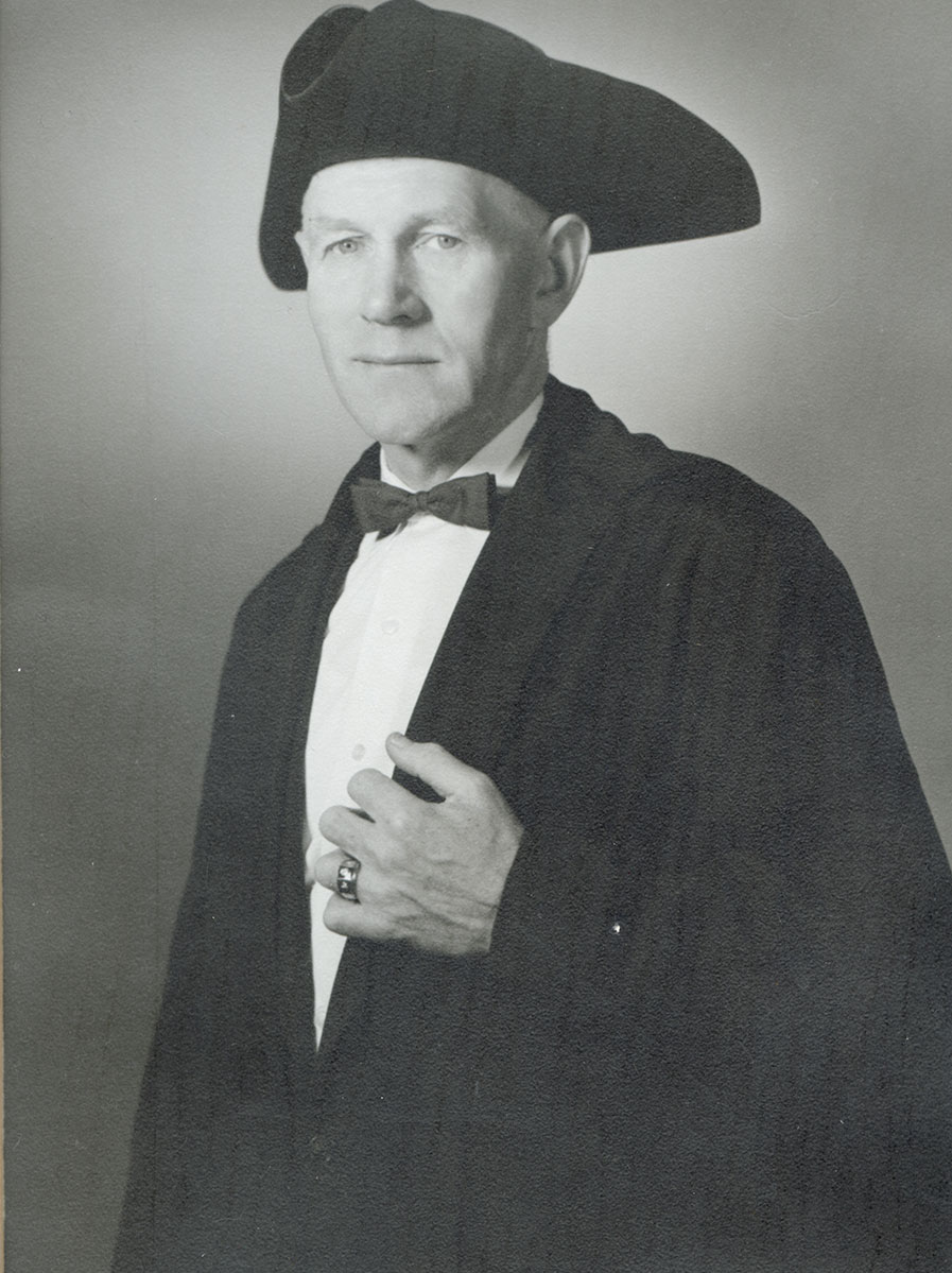 Black and white photo of white male in wardens cap and gown