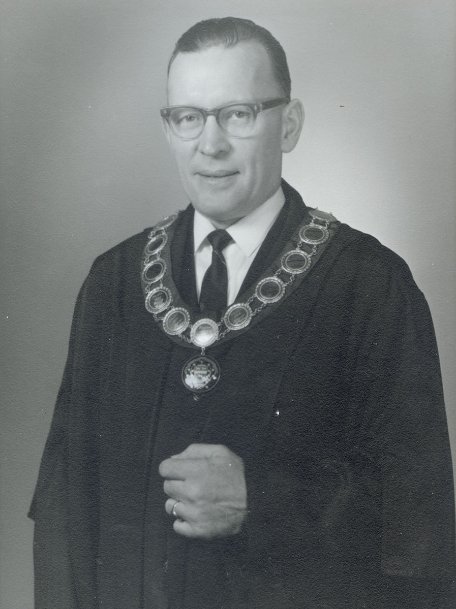 Black and white photo of white male in wardens cap and gown