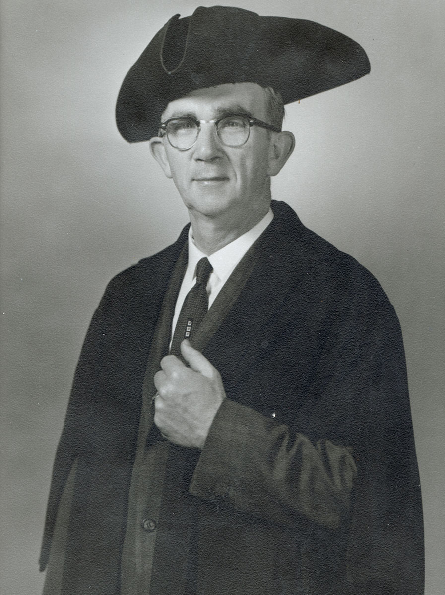 Black and white photo of white male in wardens cap and gown