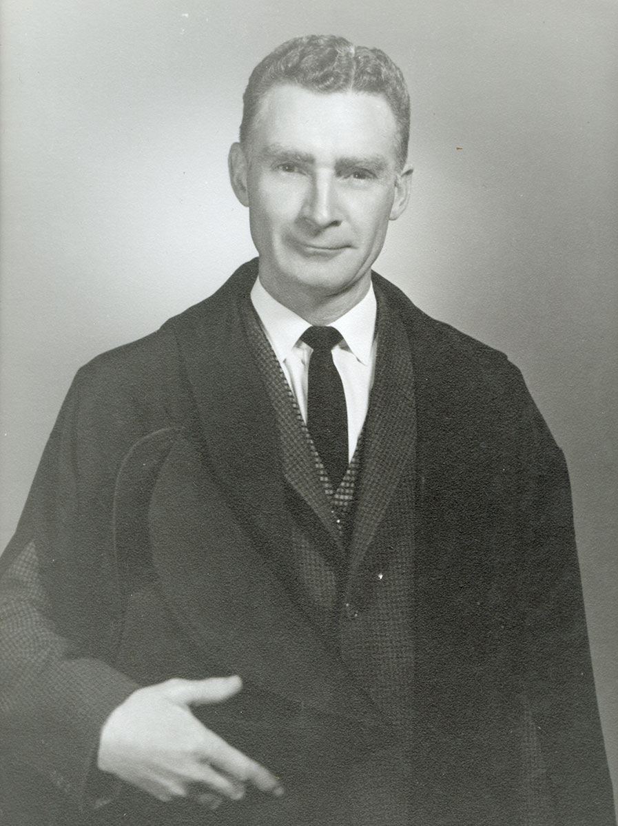 Black and white photo of white male in wardens cap and gown