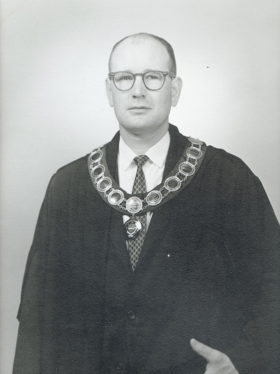 Black and white photo of white male in wardens cap and gown