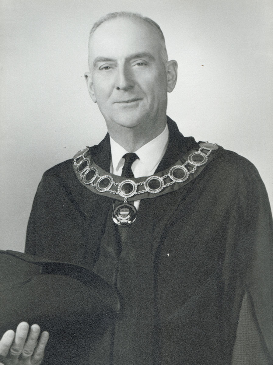 Black and white photo of white male in wardens cap and gown