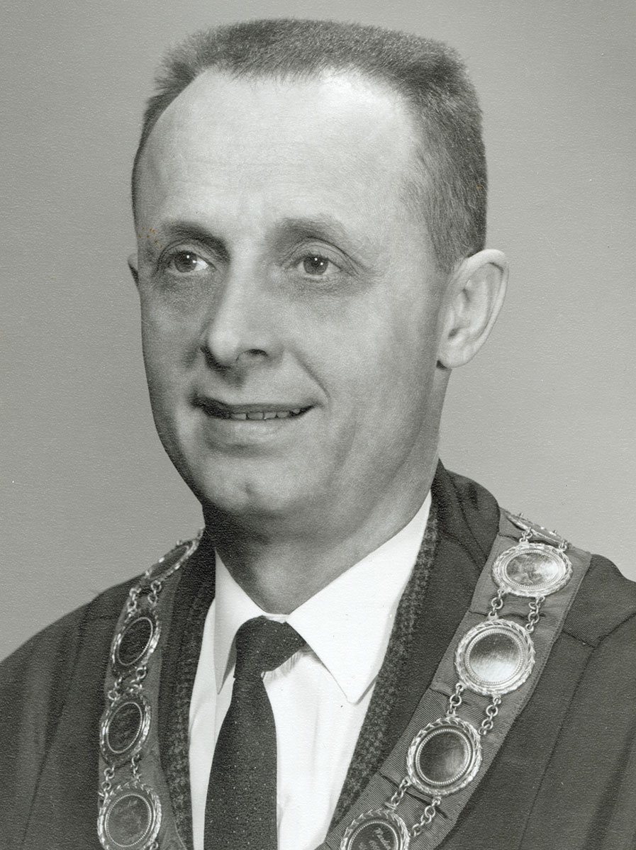 Black and white photo of white male in wardens cap and gown