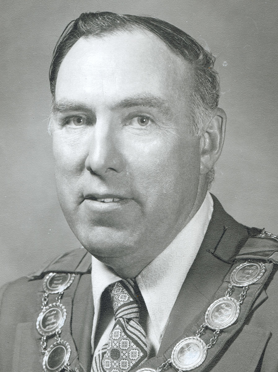 Black and white photo of white male in wardens cap and gown