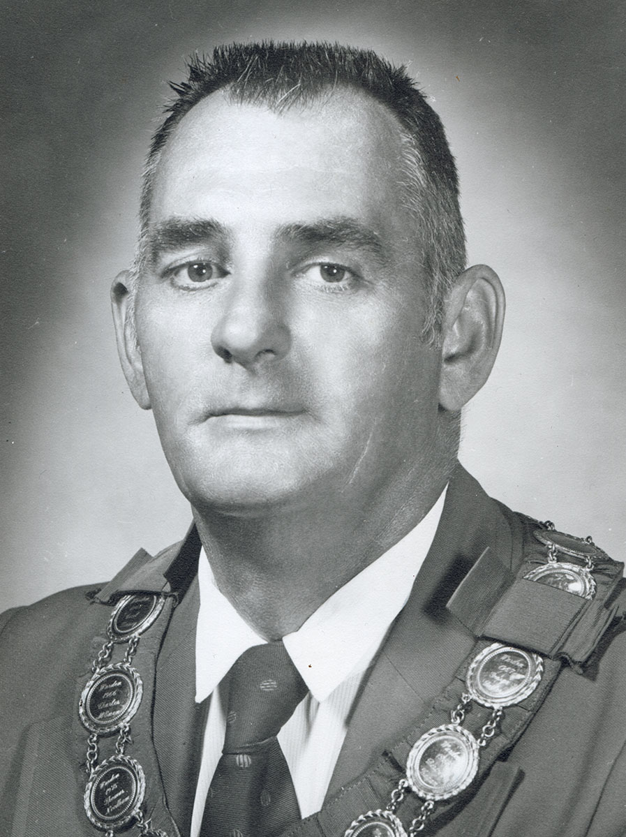 Black and white photo of white male in wardens cap and gown