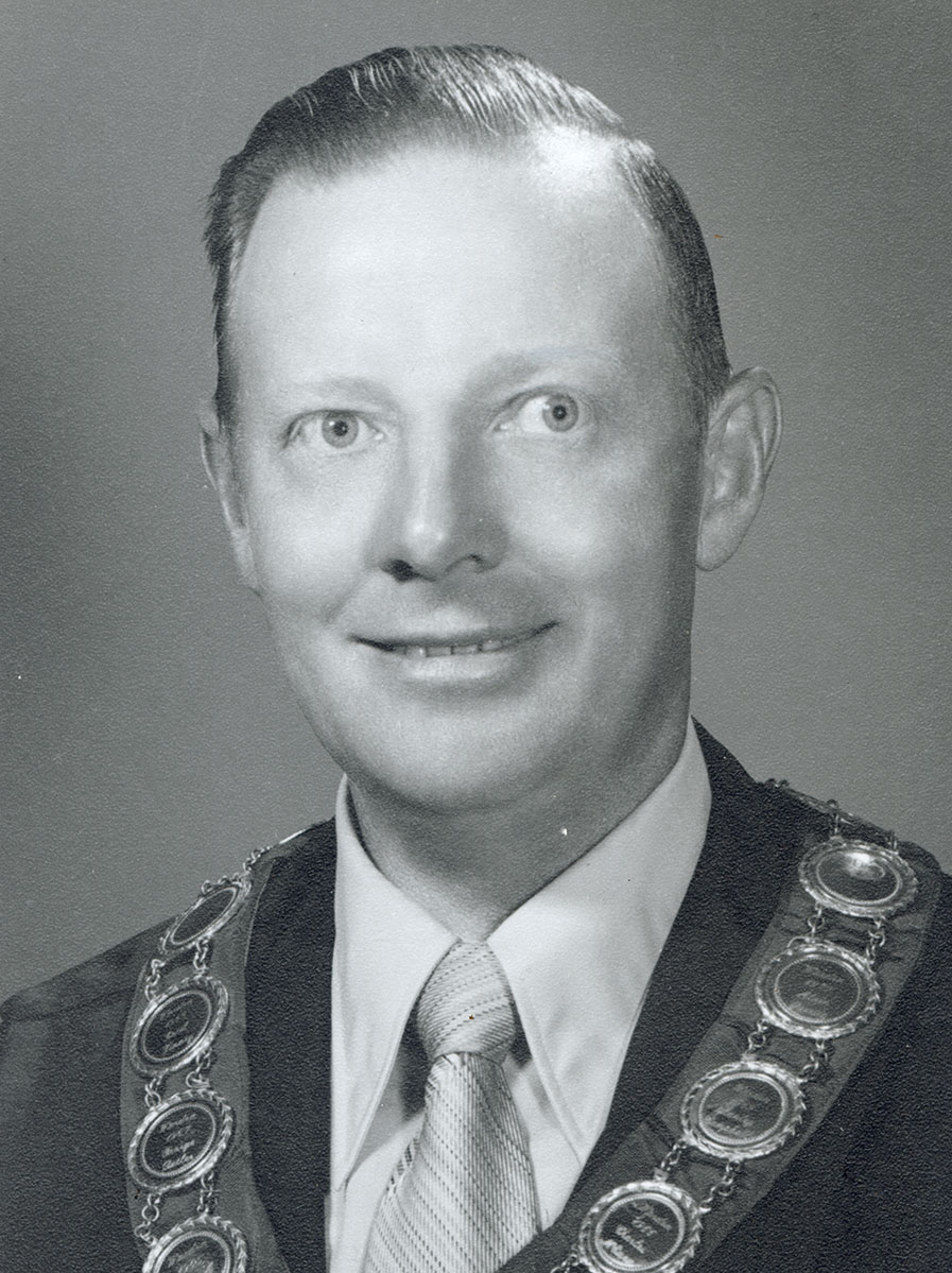 Black and white photo of white male in wardens cap and gown