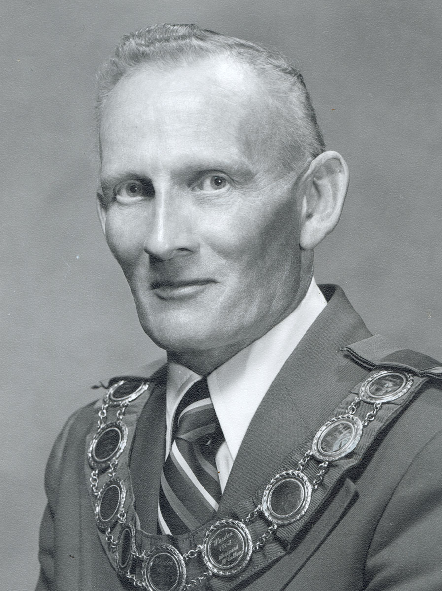 Black and white photo of white male in wardens cap and gown