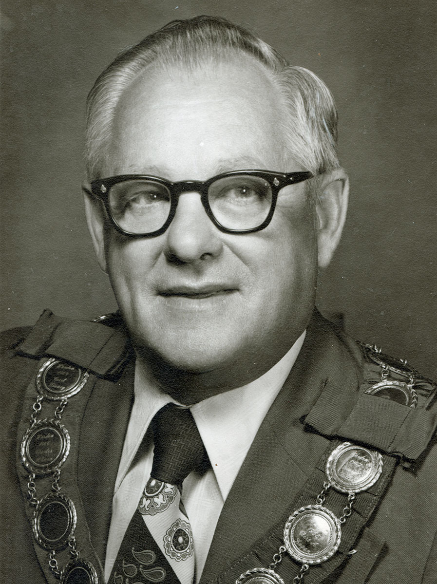 Black and white photo of white male in wardens cap and gown