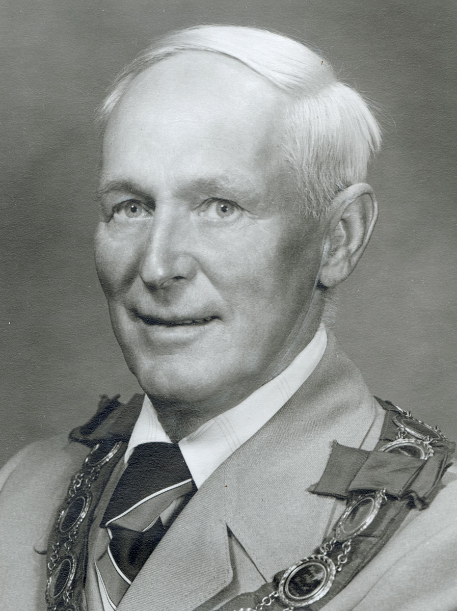 Black and white photo of white male in wardens cap and gown