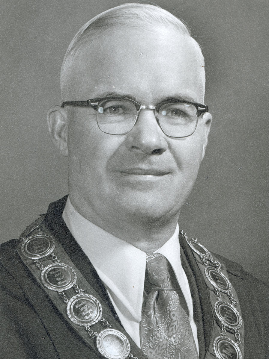 Black and white photo of white male in wardens cap and gown