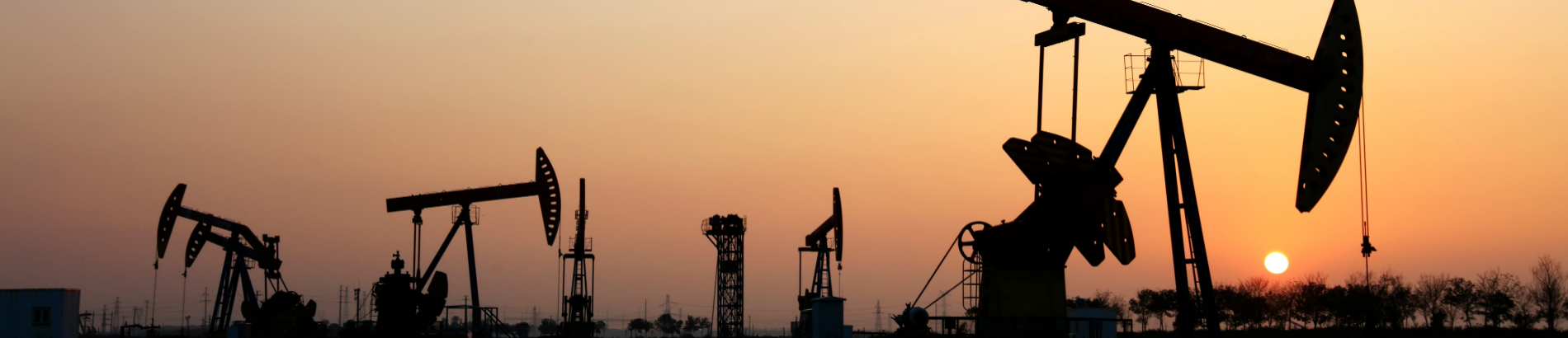 Silhouettes of oil derricks in front of a sunset