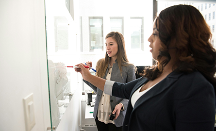 Two women writing on a glass panel