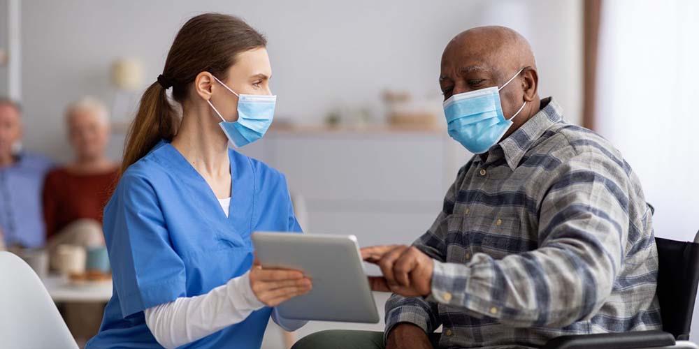 Nurse helps senior man use tablet to book appointment