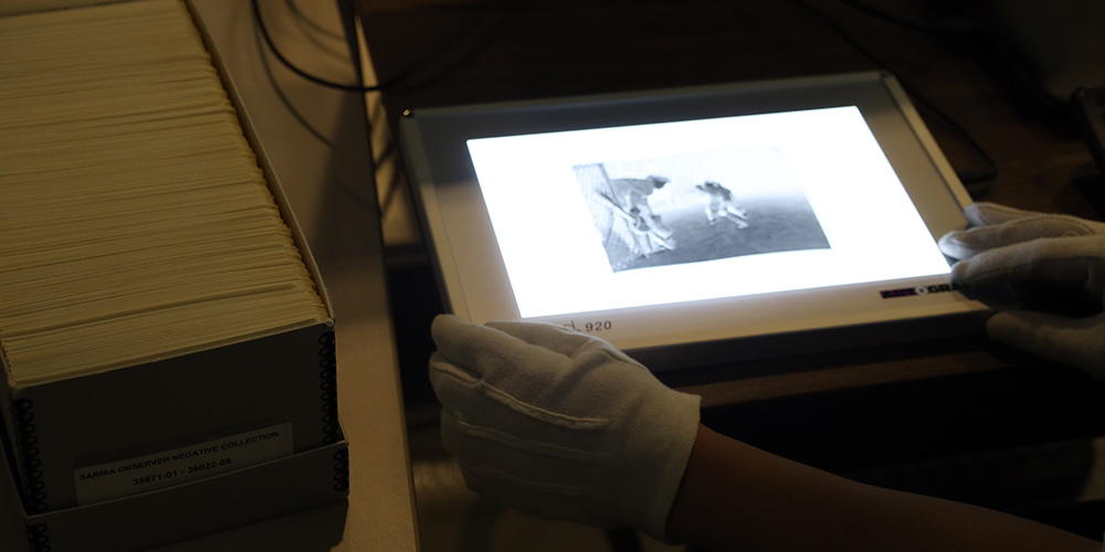 Image - A photographic negative of people playing hockey is put on a lightbox at Lambton County Archives.