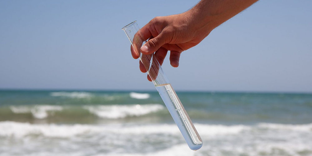 Hand holding a test tube filled with water in front of a lake