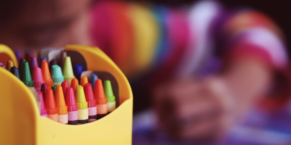 box of crayons with blurred image of child colouring in background