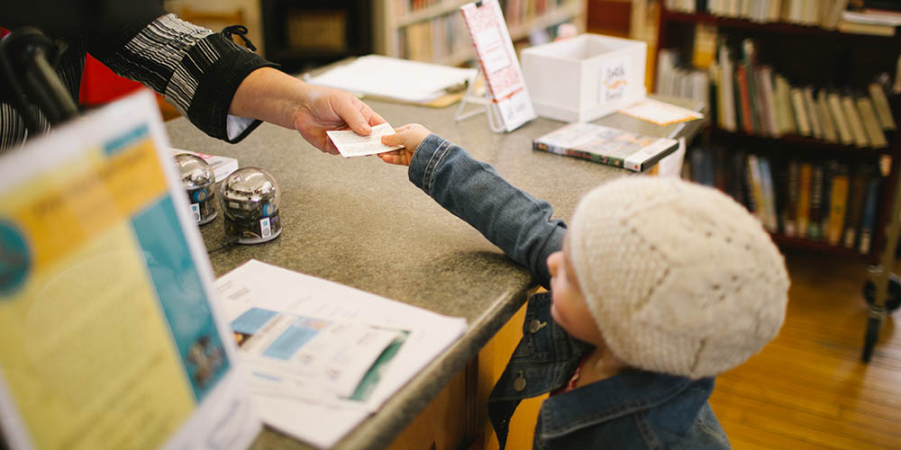 Small child passes library card to staff member across desk