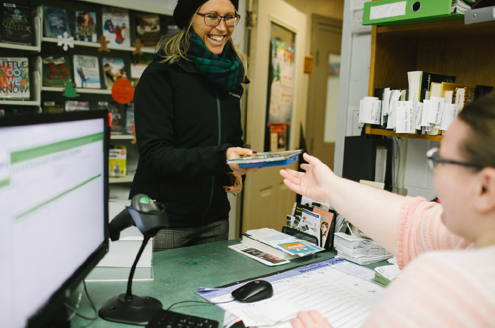 Patron passing library materials to staff member at checkout desk