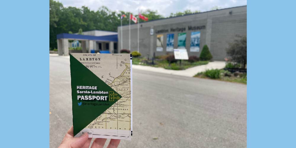 Hand holding museum passport in front of Lambton Heritage Museum