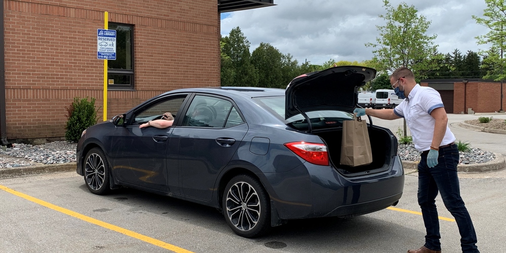 Library staff member placing materials in trunk of car waiting for curbside pickup service