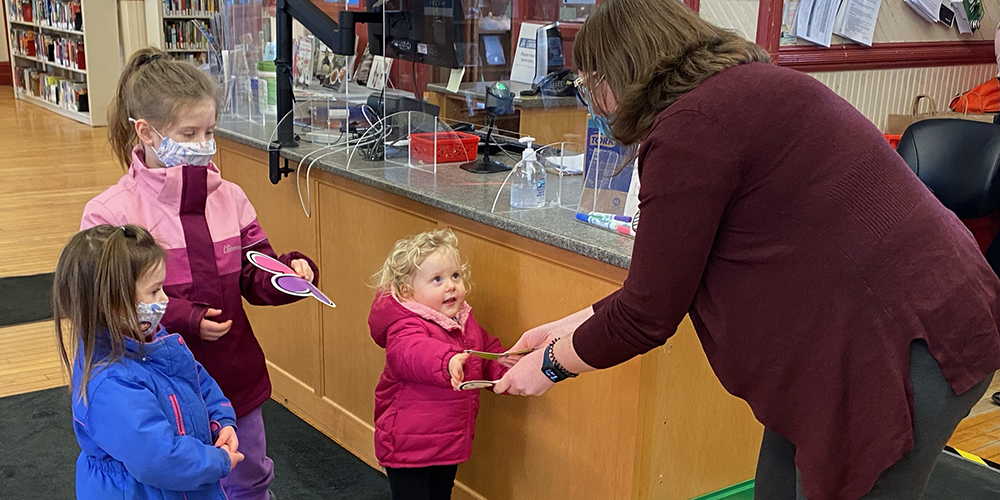 Children pass a valentines card to a library staff member