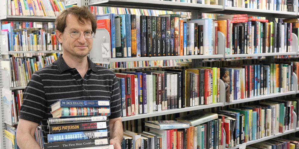 Library Technician, Paolo, holds items available for purchase at the upcoming used book sale