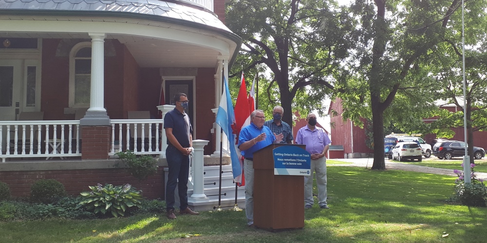 Warden Weber speaking at the SWIFT funding announcement standing in front of flags and a farmhouse.