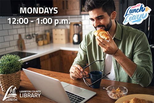 Man holding a croissant while looking at laptop