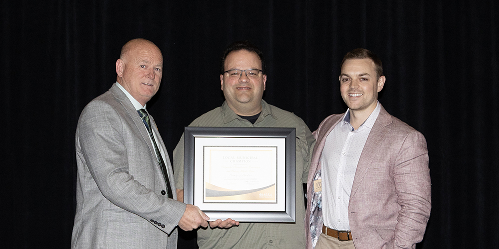 Doug Ball, Executive Director, OMSSA, presents the OMSSA Local Municipal Champion Award to County of Lambton staff Mike Konstantinou, Supervisor, Ontario Works, and Ian Hanney, Supervisor, Homelessness Prevention and Social Planning. Photo credit Sarah Bradley, iShootEvents.ca