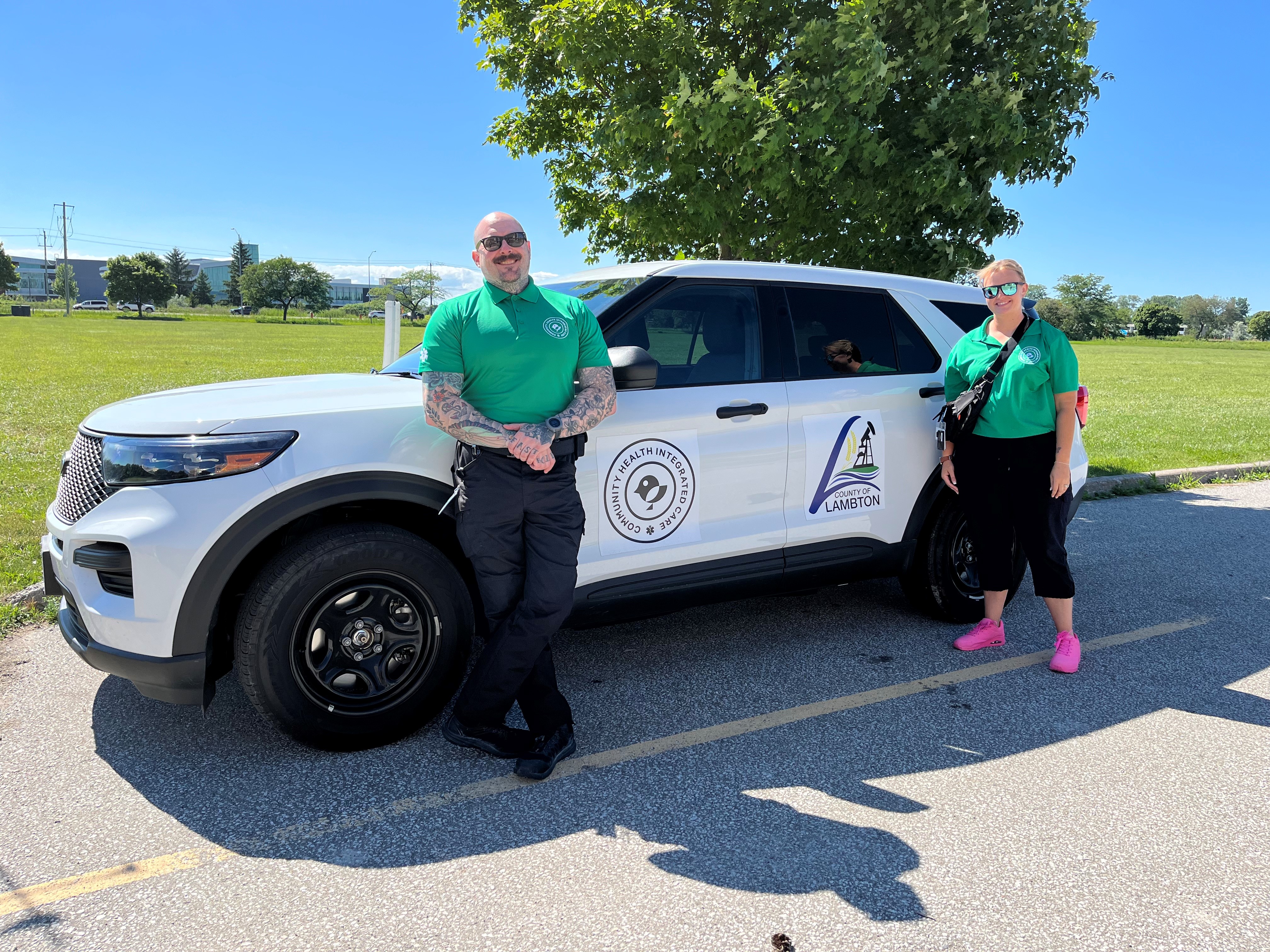 Two members of the CHIC team stand in front of a white SUV used for the program