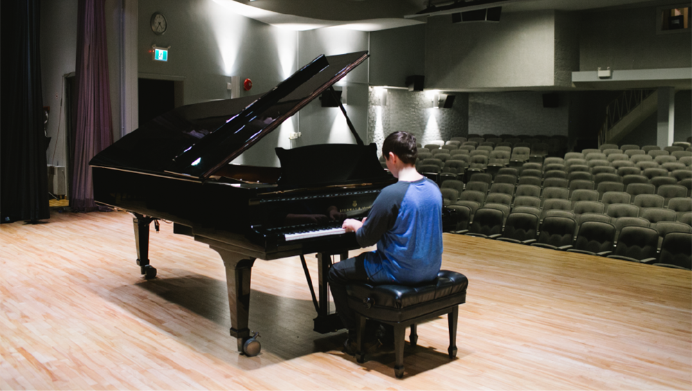 Person playing piano on stage at Sarnia Library Theatre