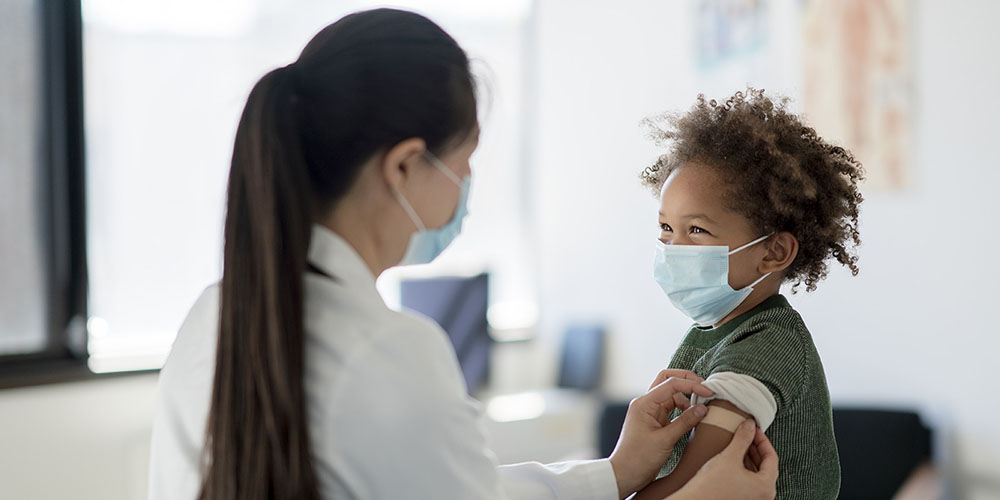 smiling child wearing a mask receives vaccination from nurse