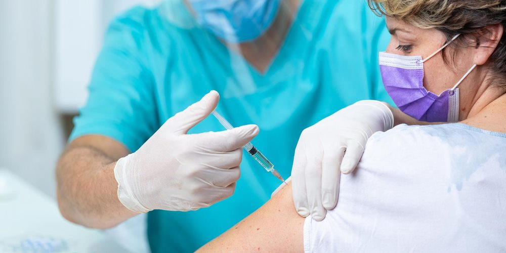 Woman wearing mask receiving flu shot from nurse